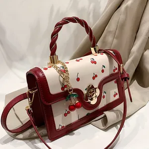 Fashionable crossbody bag with cherry print, twisted handle and floral gold clasp