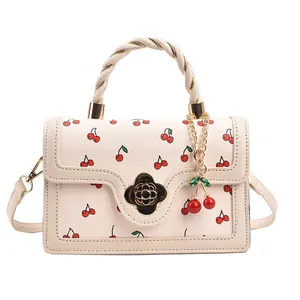 Chic cream crossbody bag with cherry print, braided handle, and gold floral clasp