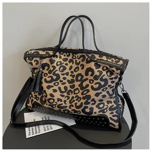 Macro detail of leopard print tote bag featuring metallic rivets and leather tassel charm