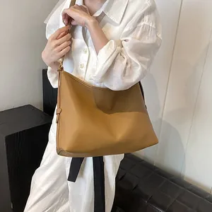 Borsa tote hobo in pelle marrone indossata da una modella su sfondo minimalista