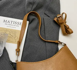 Detail of a brown matte leather half-moon bag with adjustable strap on a gray blazer background