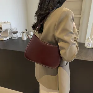 Close-up of a vintage burgundy leather crescent shoulder bag styled with a professional suit