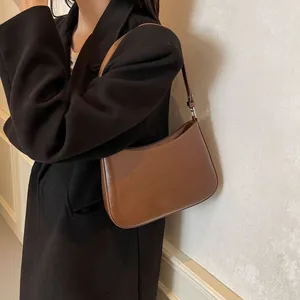 Detail of a brown leather crescent shoulder bag with silver buckles and smooth texture