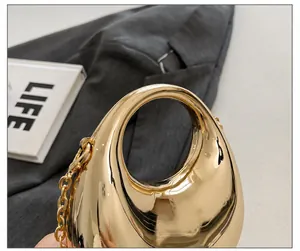 Detail of high-gloss gold crescent mini bag with integrated handle and metal chain