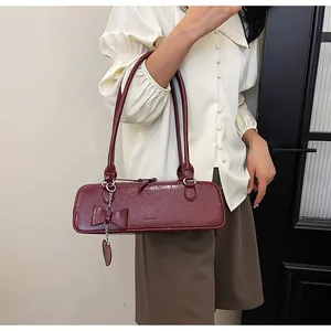 Dettaglio della borsa baguette bordeaux con fiocco e ciondolo a cuore su beige