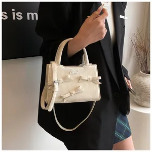 Détail d'un sac à main blanc crème orné de trois nœuds décoratifs et du logo en métal Chord