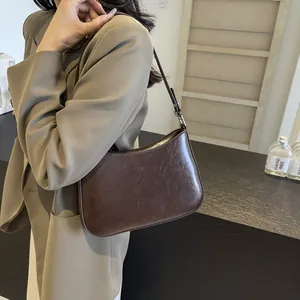 Detail of a dark brown half-moon underarm bag in glossy leather worn by a model