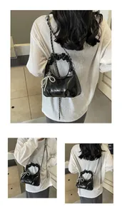 Detail view of black glossy pleated handbag with chain strap and pearl bow charm