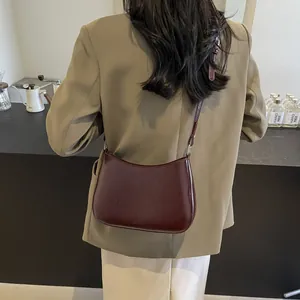Outdoor shot of a burgundy crescent crossbody bag with embossed lettering on smooth leather
