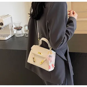 Detail of white embossed leather handbag with gold hardware and pink plush charm