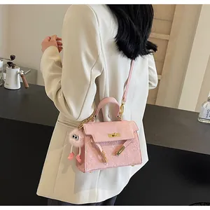 Detail of pink Kelly style handbag with embossed pattern and plush charm on white blazer
