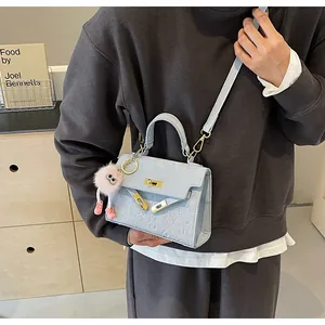 Detailed shot of light blue crossbody bag with cartoon embossing and a pink plush charm