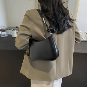 Detail of glossy black leather moon bag with KIMIIN logo worn by a model in a cafe
