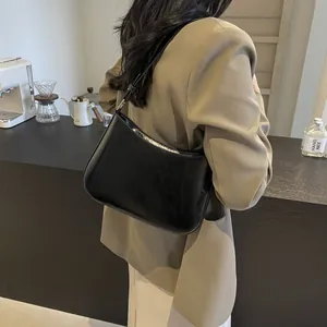 Detail of minimalist black glossy leather underarm bag with silver buckles on a casual outfit
