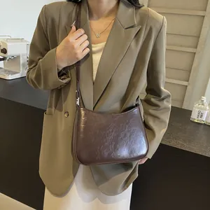 Dark brown half-moon crossbody bag in wax-finish leather shown on model in a cafe setting