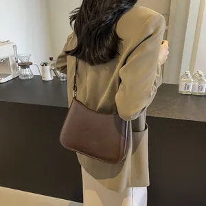 Minimalist brown leather underarm bag worn with casual autumn outfit in coffee shop scene