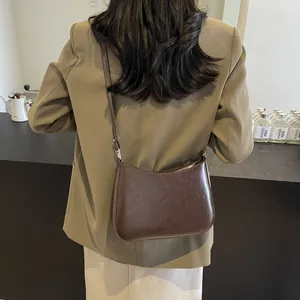 Brown leather crescent shoulder bag styled with an elegant cafe aesthetic background