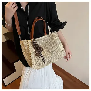 Detail van strandtas van stro met franjes en bruine leren schouderriem