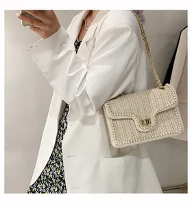 Dettaglio borsa a tracolla beige intrecciata con bordo di perle e catena dorata