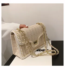 Dettaglio borsa in paglia beige con decoro di perle e tracolla a catena dorata