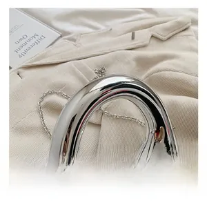 Makro-Detail der silbernen Acryl-Clutch mit asymmetrischem Rundgriff und Metallkette