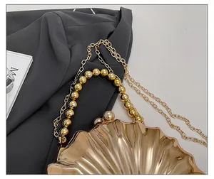 Detail view of a gold shell evening bag with radial texture and fine chain strap