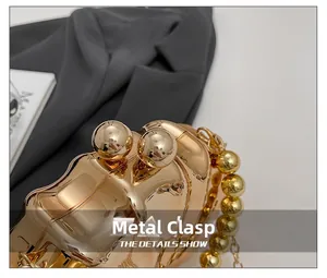 Detail of elegant gold metal evening bag featuring a spherical hardware clasp and chain