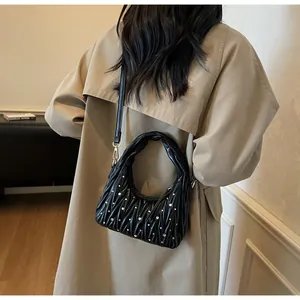 Detailed view of black pleated shoulder bag with silver rhinestones on a beige coat