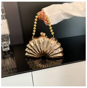 Detail showing the polished golden shell-shaped clutch bag with elegant bead handle
