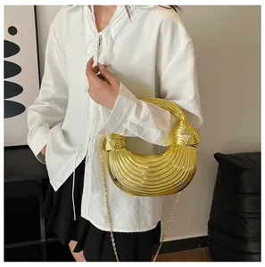 Detail of a metallic gold crescent bag with textured pleats held by a model in a white shirt