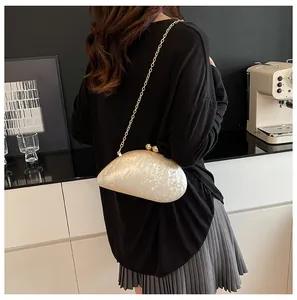Detail of creamy acrylic evening clutch with pearlescent texture and gold chain strap