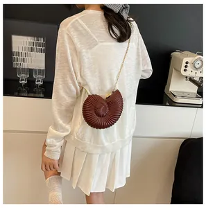Détail du sac nautile marron foncé avec chaîne dorée porté par un mannequin chic