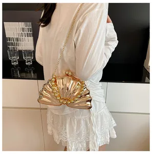 Shell-shaped gold evening clutch bag with pearl trim and chain strap shown on model