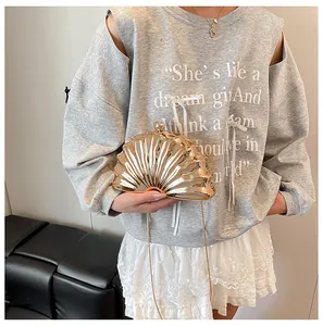 Golden shell-shaped evening bag with metallic finish shown held by a model with chain