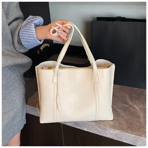 Detail of cream large-capacity tote bag with pebbled texture and vertical straps on stone surface
