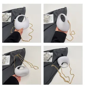 Detailweergave van witte halfronde acryl handtas met gouden ketting en ronde handgreep