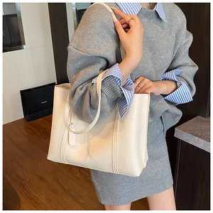 Detail of a large cream tote bag with lychee texture and stitching on a female model