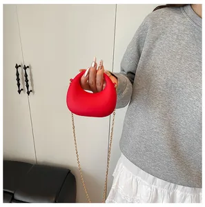 Detailweergave van rode halvemaanvormige handtas met goudkleurige ketting en matte finish