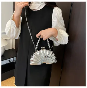 Silver shell clutch bag worn by model, featuring metallic finish and pearl bead handle
