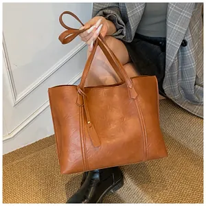 Detail of a large brown tote bag showing smooth PU leather texture and shoulder strap