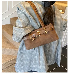 Sac bandoulière en daim marron avec boucle dorée porté par un mannequin chic