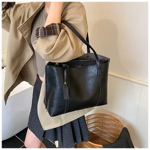 Close-up of minimalist black leather tote bag worn by model in a natural indoor setting