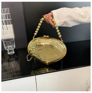 Détail du sac de soirée doré en forme de coquille avec poignée perlée et fini brillant