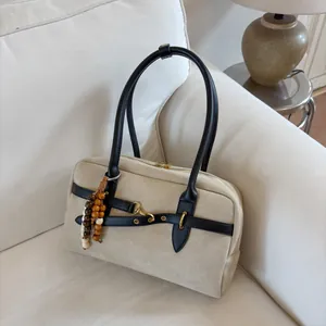 Detail of minimalist beige crossbody bag with wooden bead charm on a soft white sofa