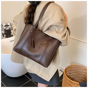 Detail of a large brown tote bag on model, featuring parallel stitching and long strap charm