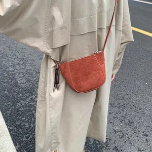 Detail einer rostroten Wildleder-Umhängetasche an einem Model in einem beigen Trenchcoat
