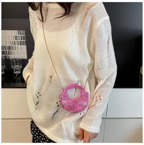 Detail der metallisch-pinken Halbmondtasche mit Goldkette auf weißem Strickoutfit