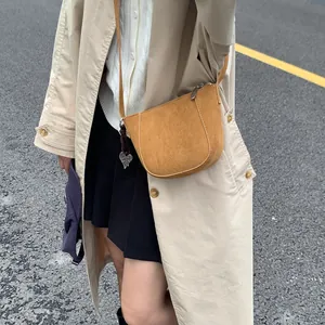 Nahaufnahme der braunen Wildleder-Satteltasche mit silbernem Herzanhänger am Model