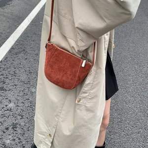 Detailansicht der dunkelroten Wildleder-Halbmondtasche getragen über einem beigen Trenchcoat