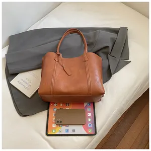 Brown leather tote bag showing large capacity for laptop and daily essentials on a suit
